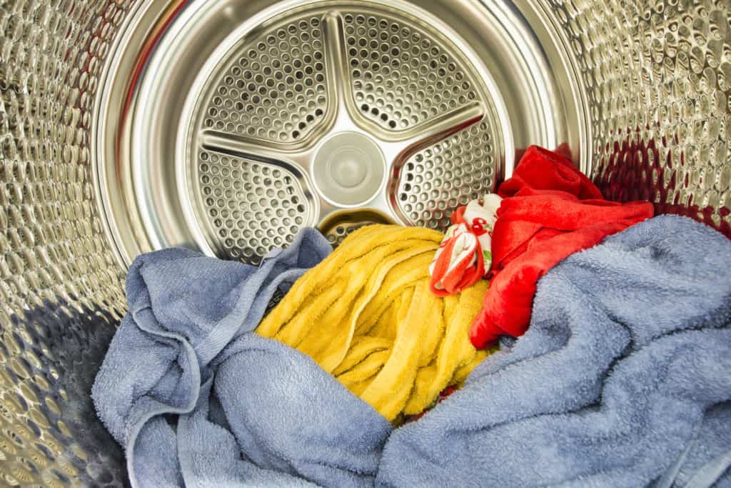 Inside view of a washing machine drum with a blue towel, yellow cloth, and red fabric. The fabrics are rumpled together, and the stainless steel drum interior is visible.